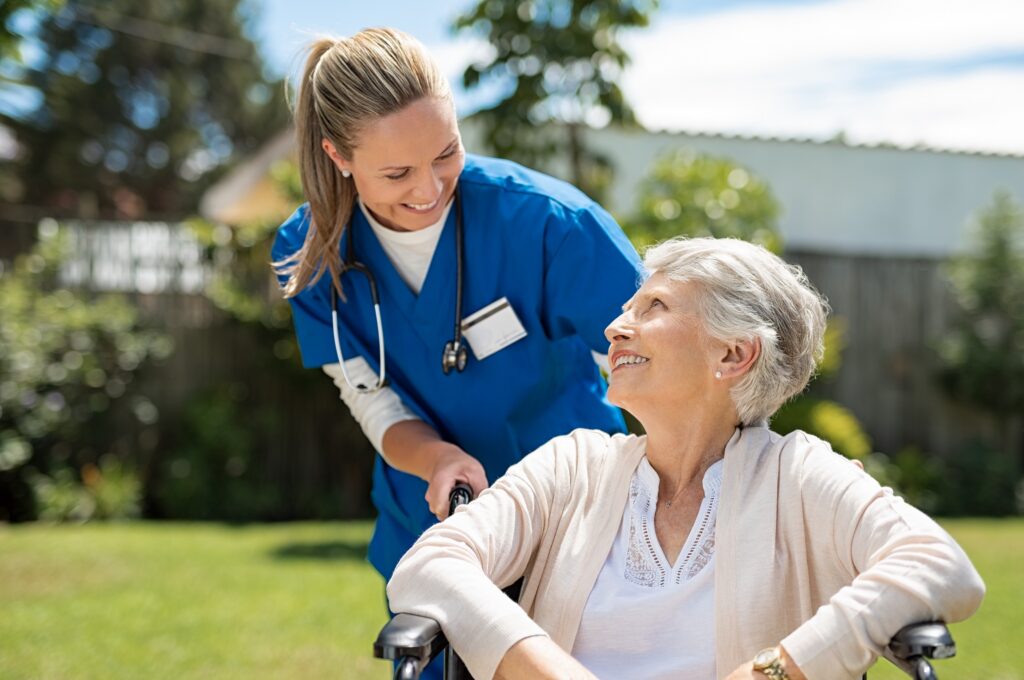 Nurse taking care of old woman in wheelchair outdoor.